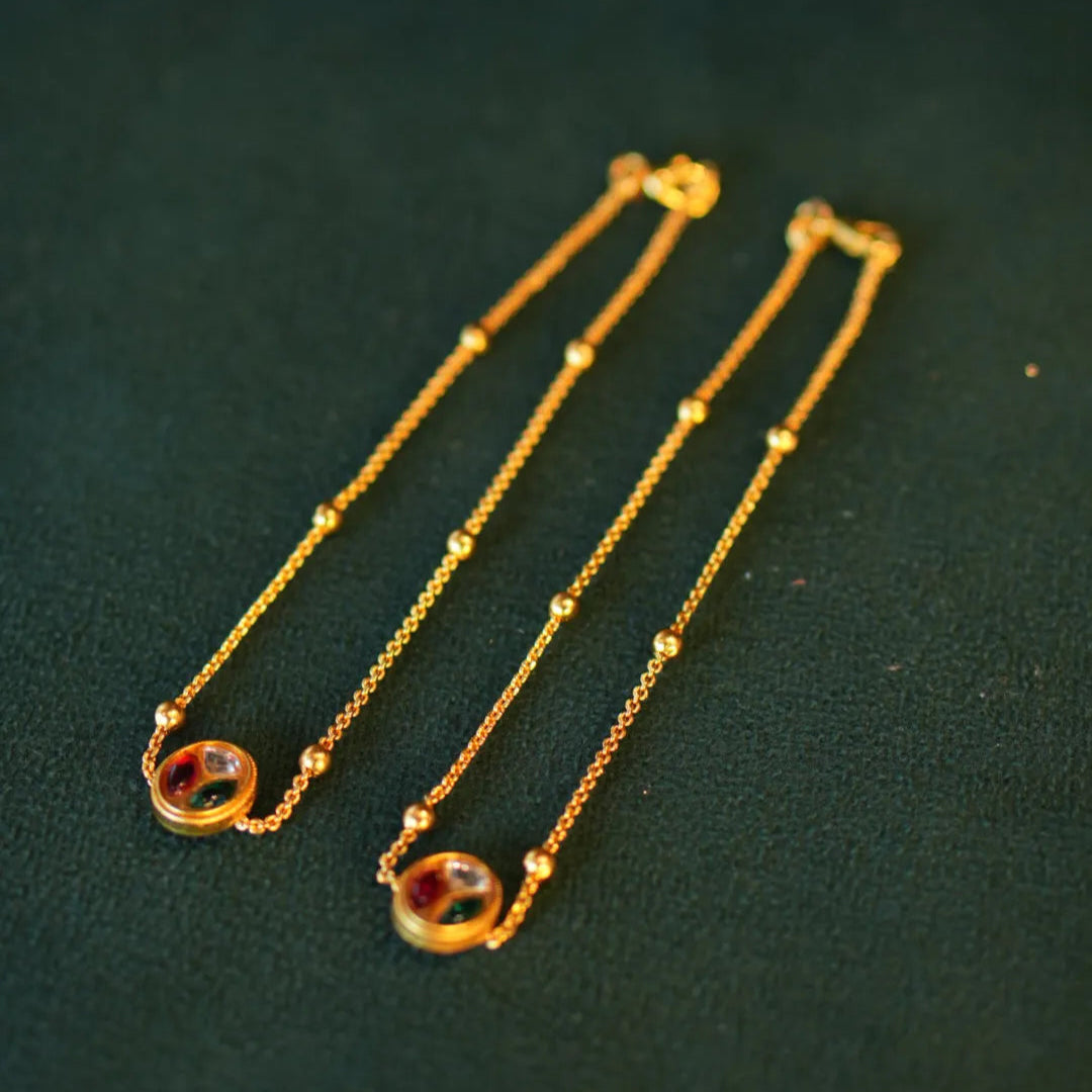 Two gold necklaces with colored stones on a dark green background