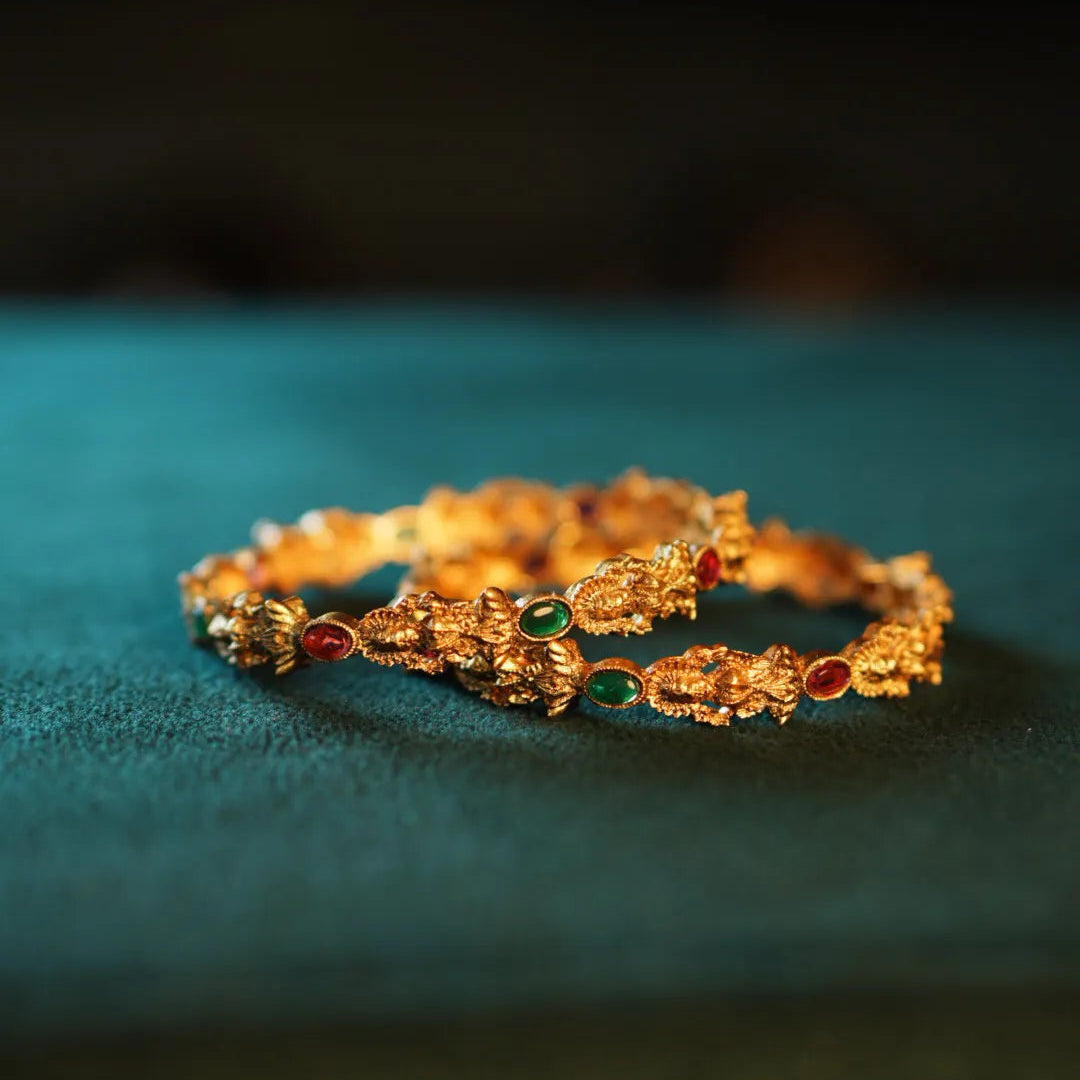 Gold bracelet with gemstones on a teal surface