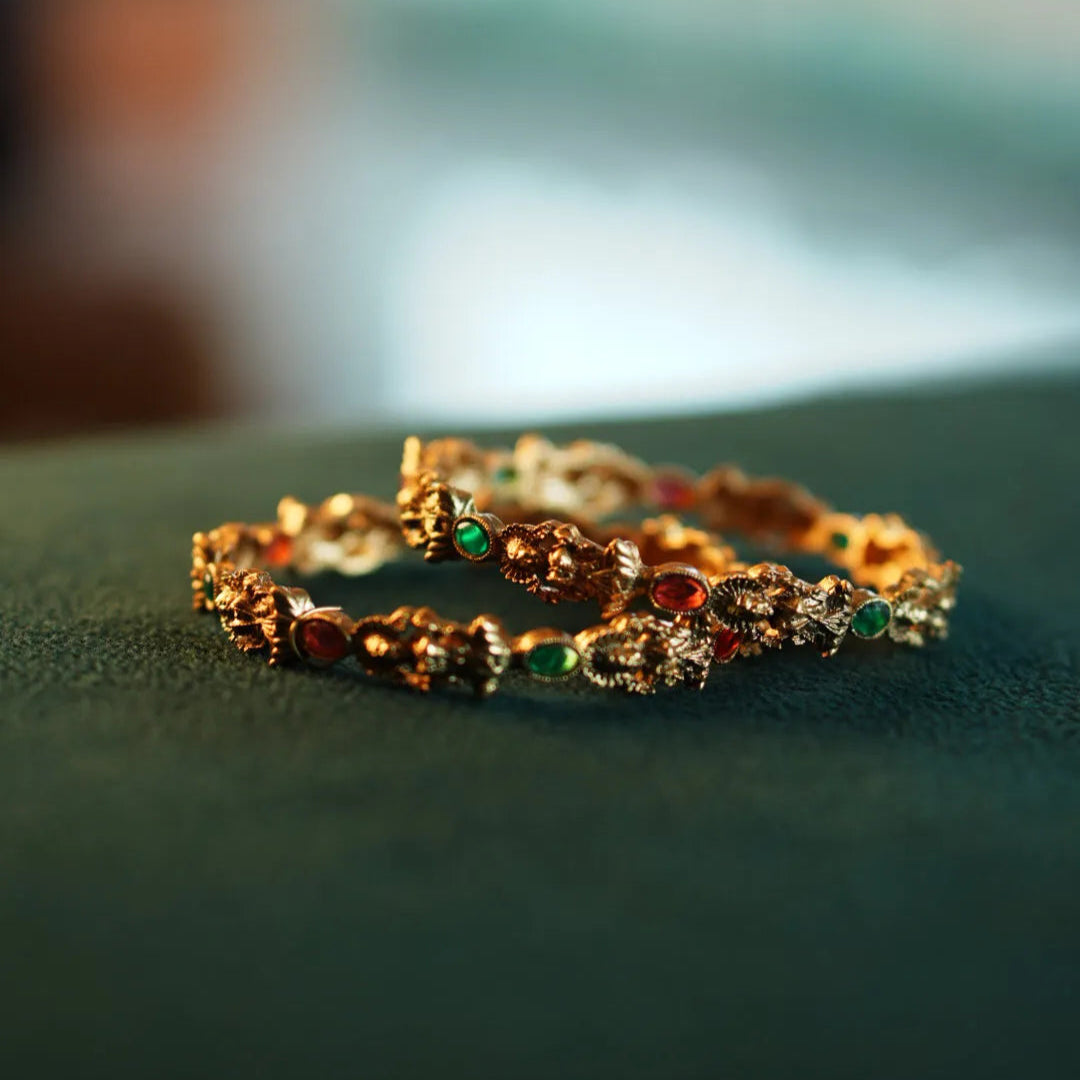 Gold bracelets with gemstones on a green surface