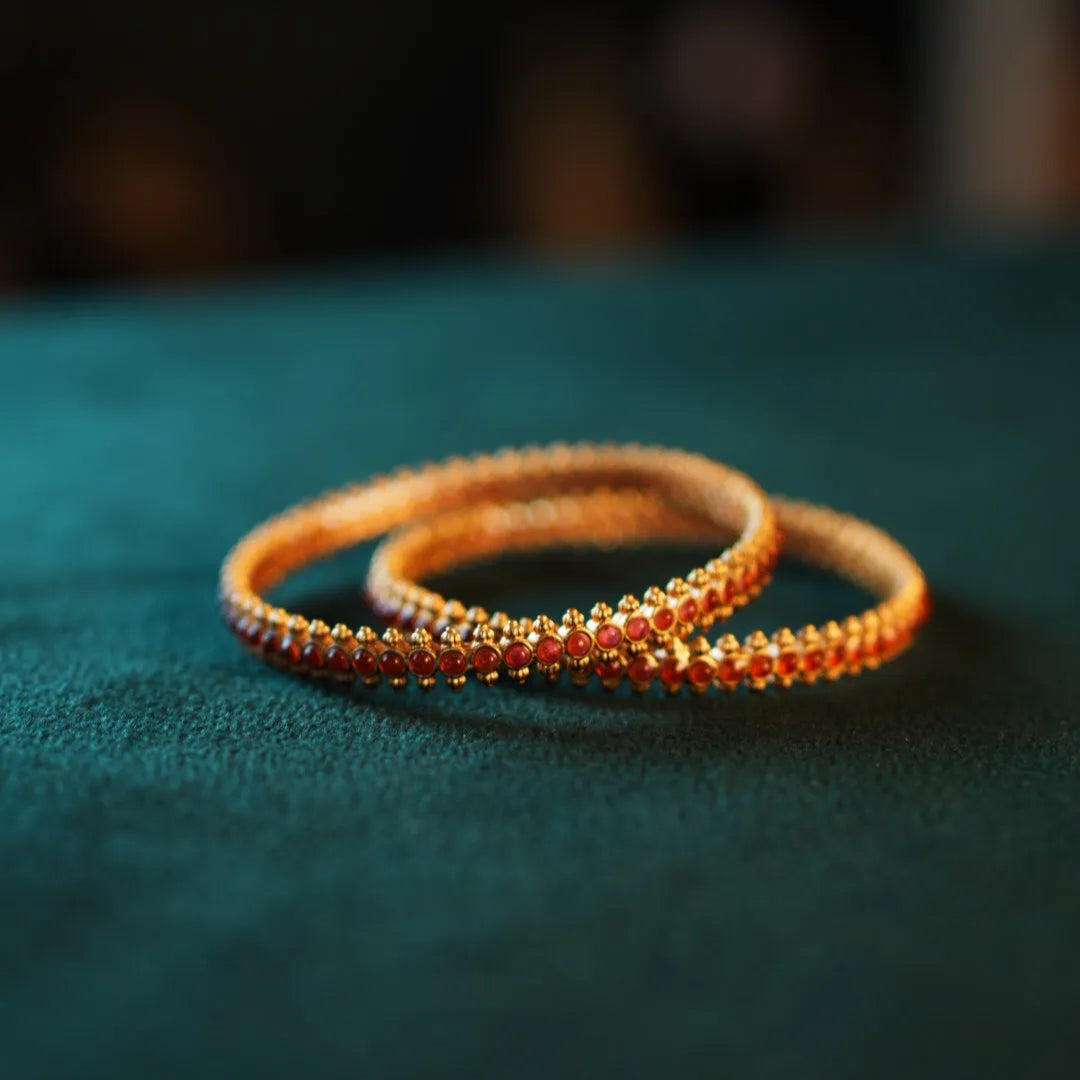 Two orange beaded bracelets on a dark green surface with a blurred background