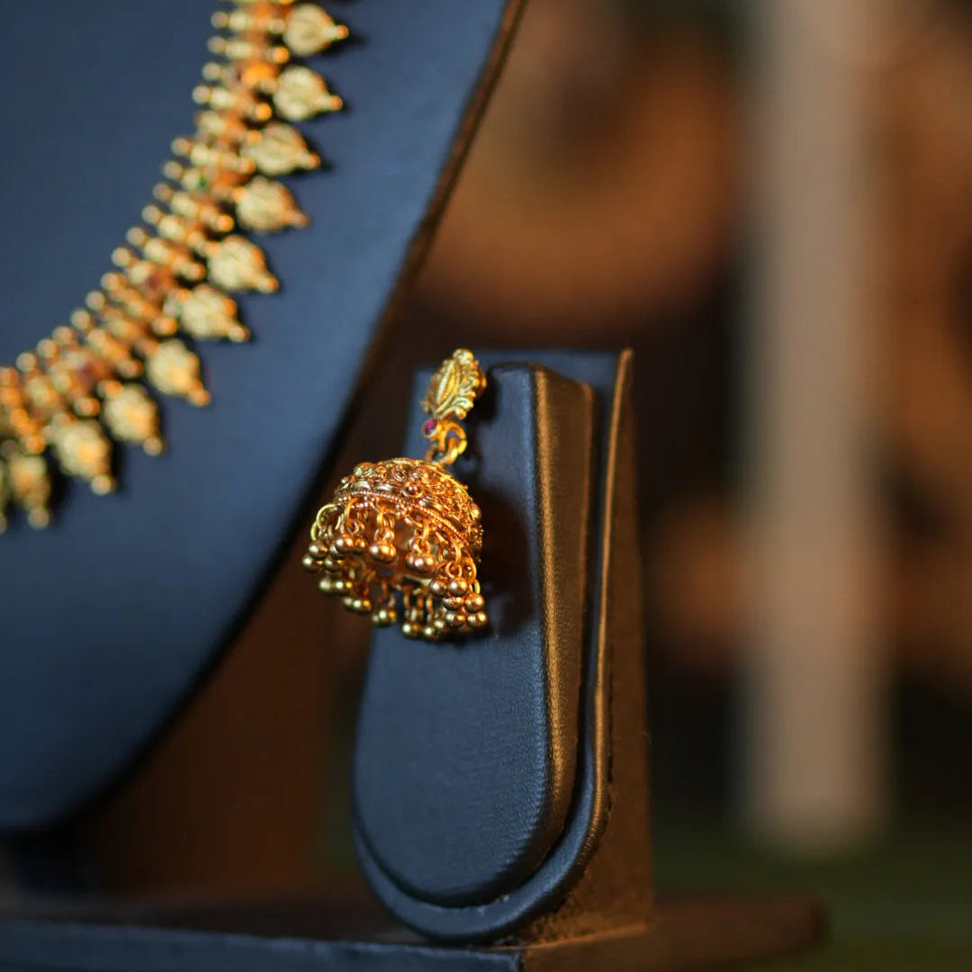 Gold necklace and earring set on a blue stand with a blurred background