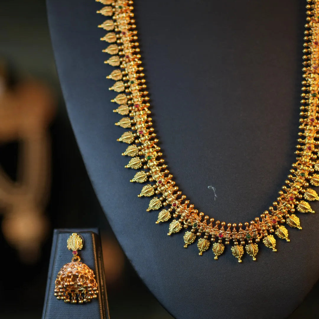 Gold necklace and earring set on a dark stand