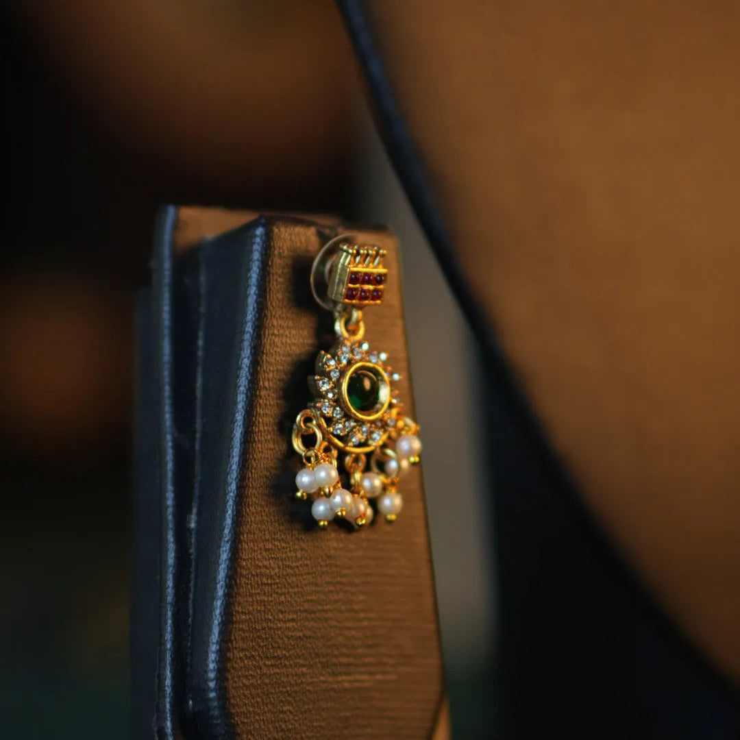 Gold earring with green gemstone on a brown stand