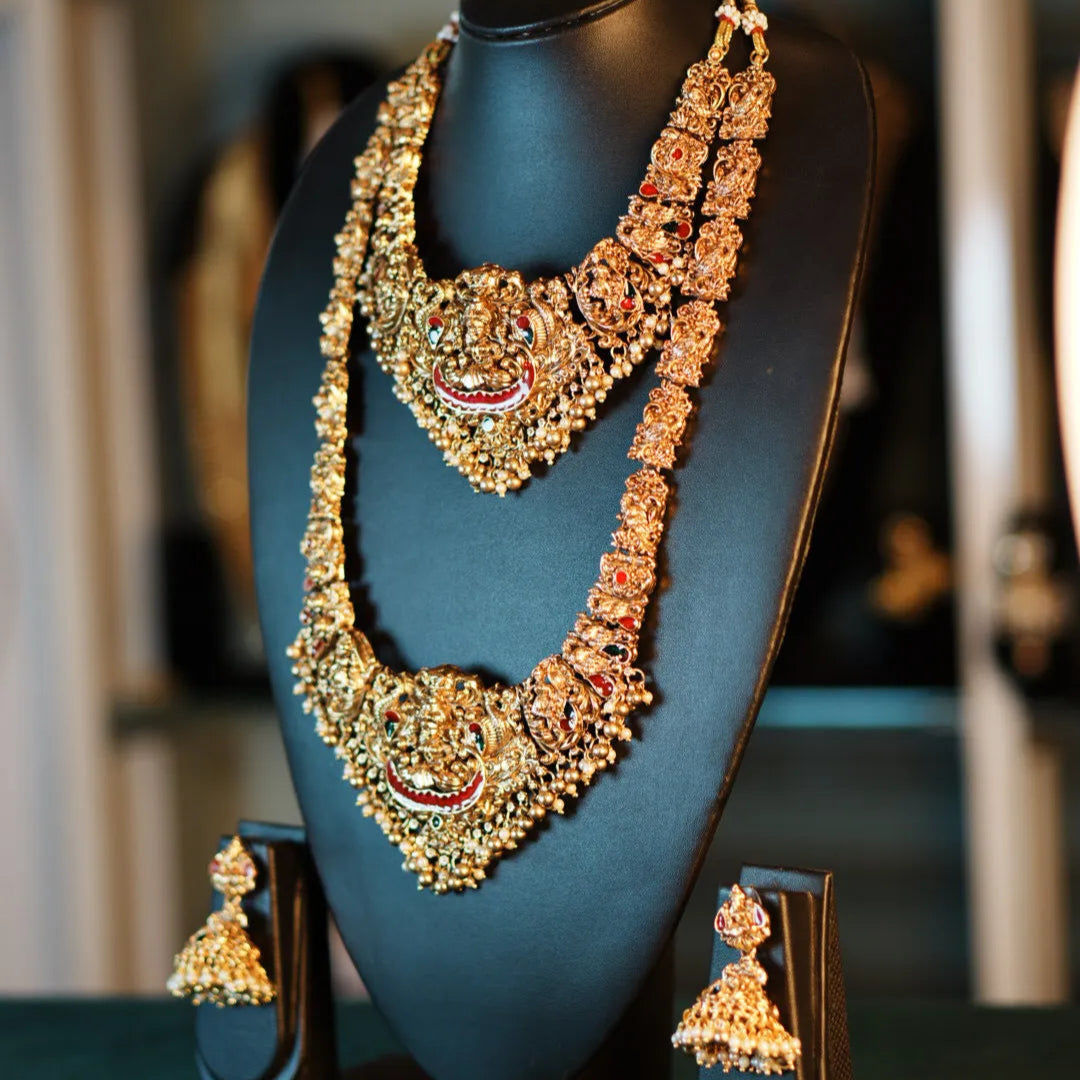 Ornate gold and green necklace with matching earrings on a black stand.