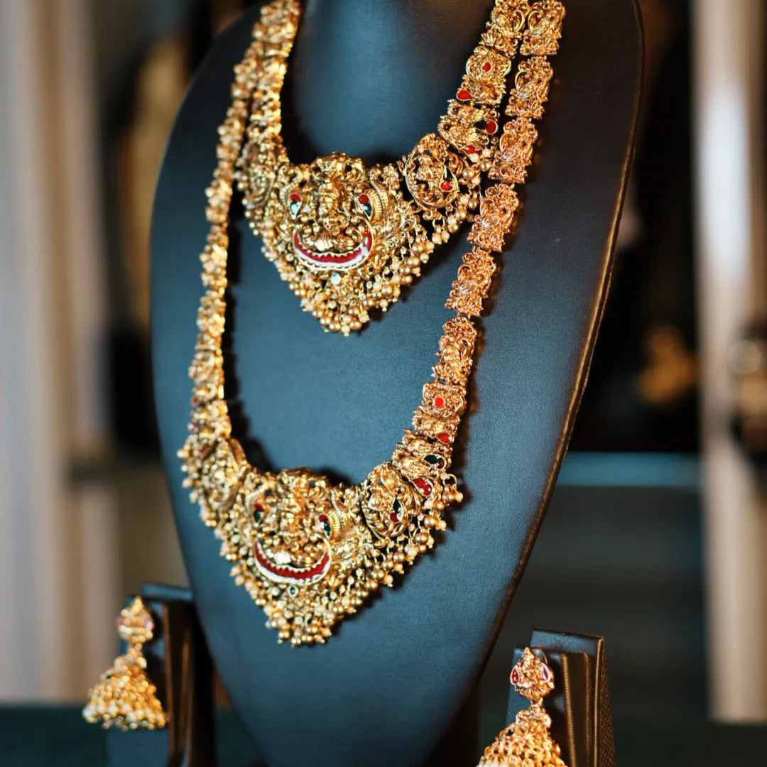 Ornate gold necklace and earrings on a black stand with a blurred background