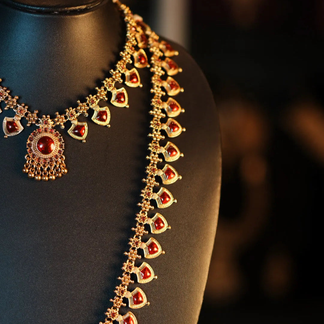 Ornate necklace with red stones on a black mannequin against a dark background