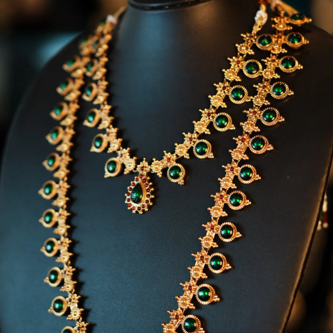 Gold necklace with green gemstones on a black mannequin