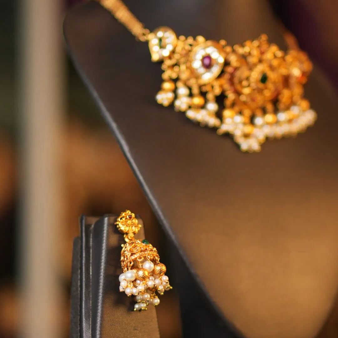 Gold jewelry set with earrings and necklace on a dark stand.