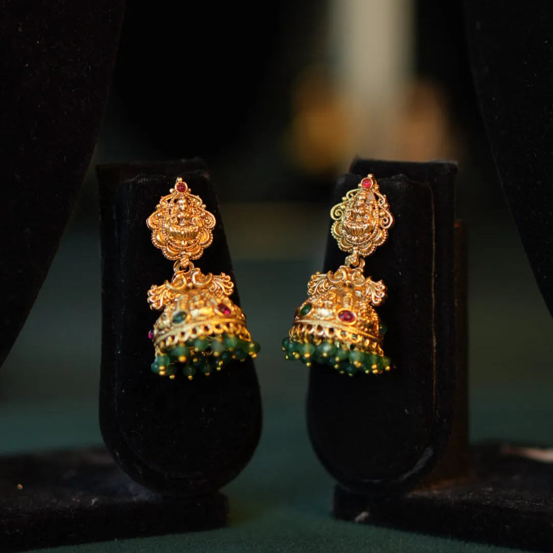 Gold and green earrings on black stands with a blurred background