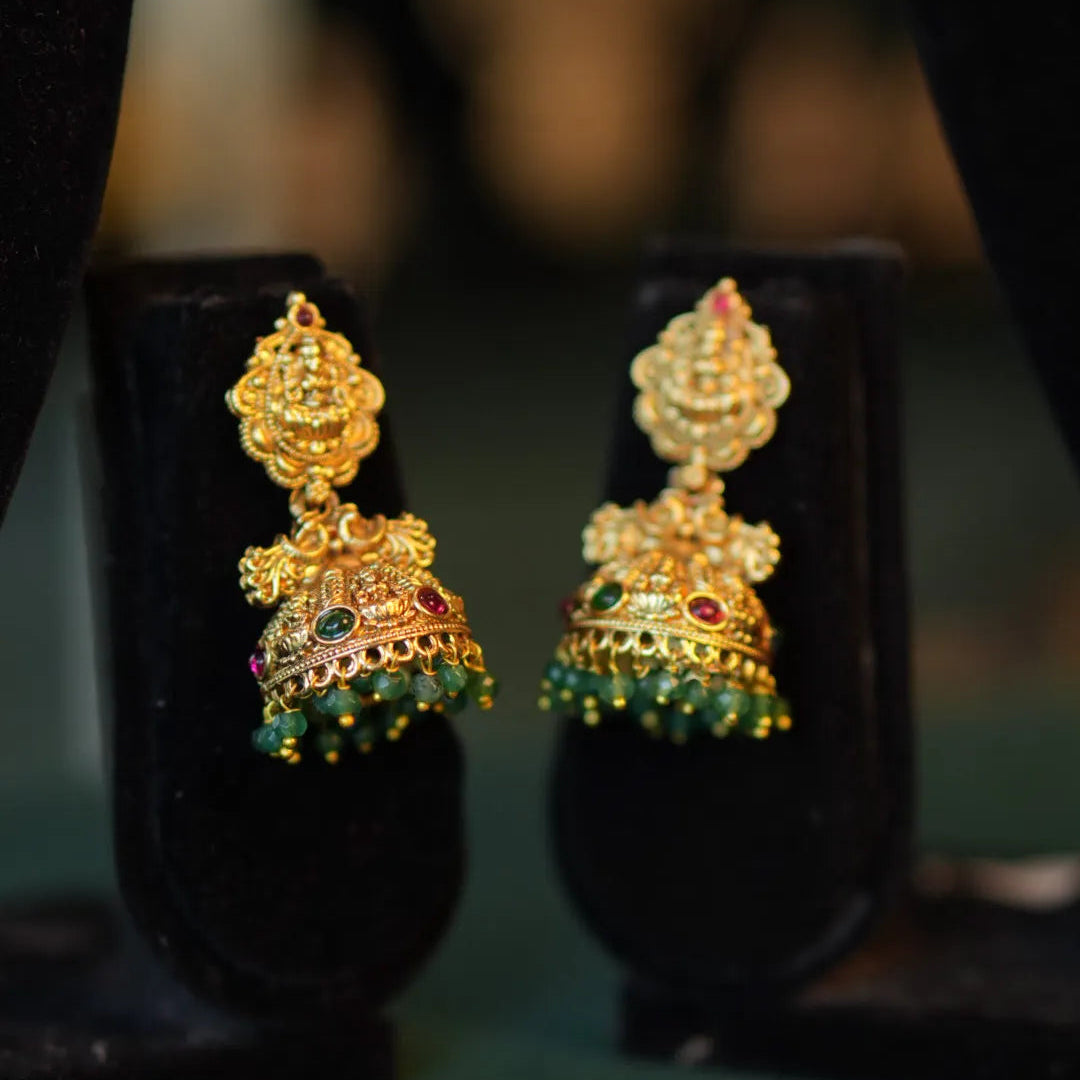 Gold earrings with green gemstones on black stands