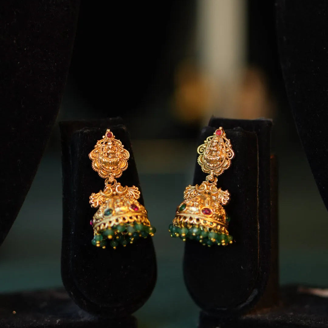 Gold earrings with green gemstones on black stands against a dark background