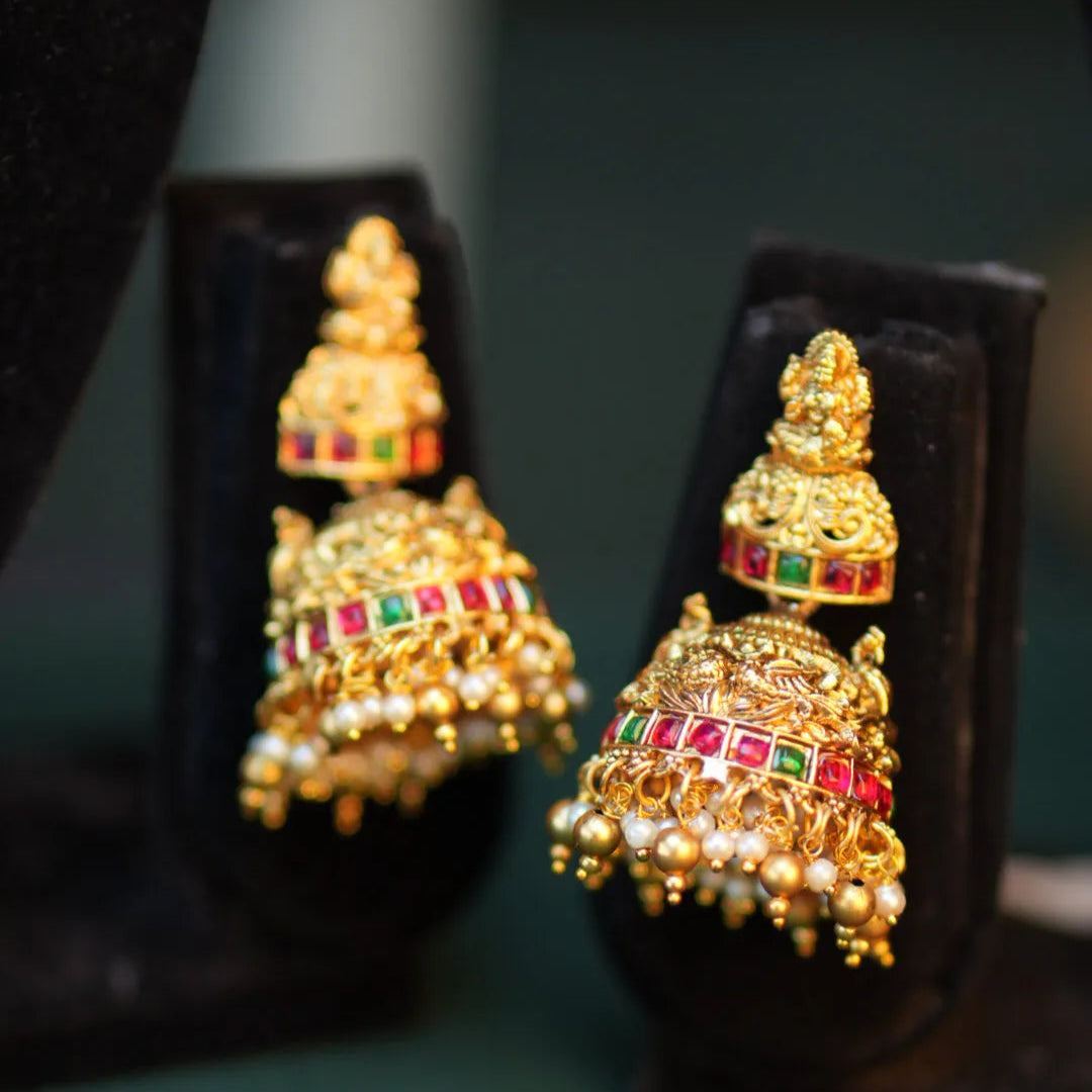 Gold earrings with red and green gemstones on black stands against a dark background