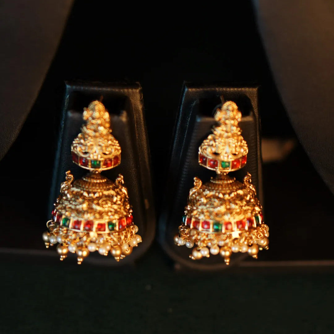 Pair of gold earrings with gemstones in a clear display case on a black background