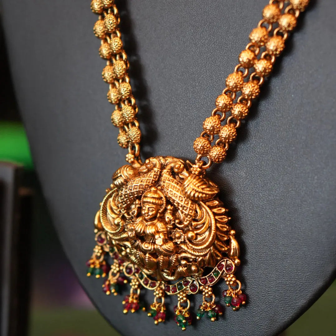 Gold necklace with a detailed pendant on a gray stand