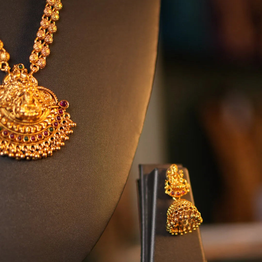 Gold necklace and earrings on a stand with a blurred background