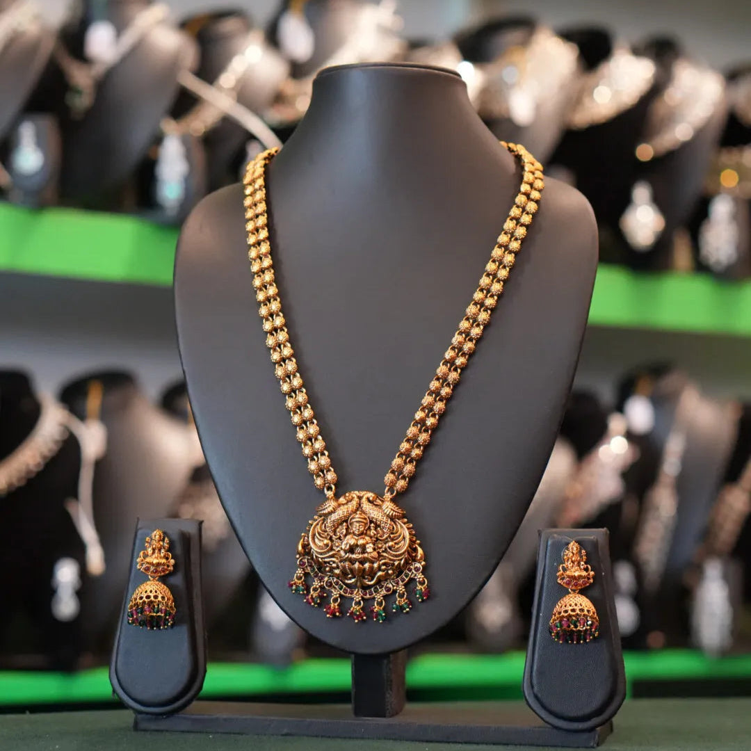 Gold necklace and earrings on a mannequin bust with a blurred background of shoes.