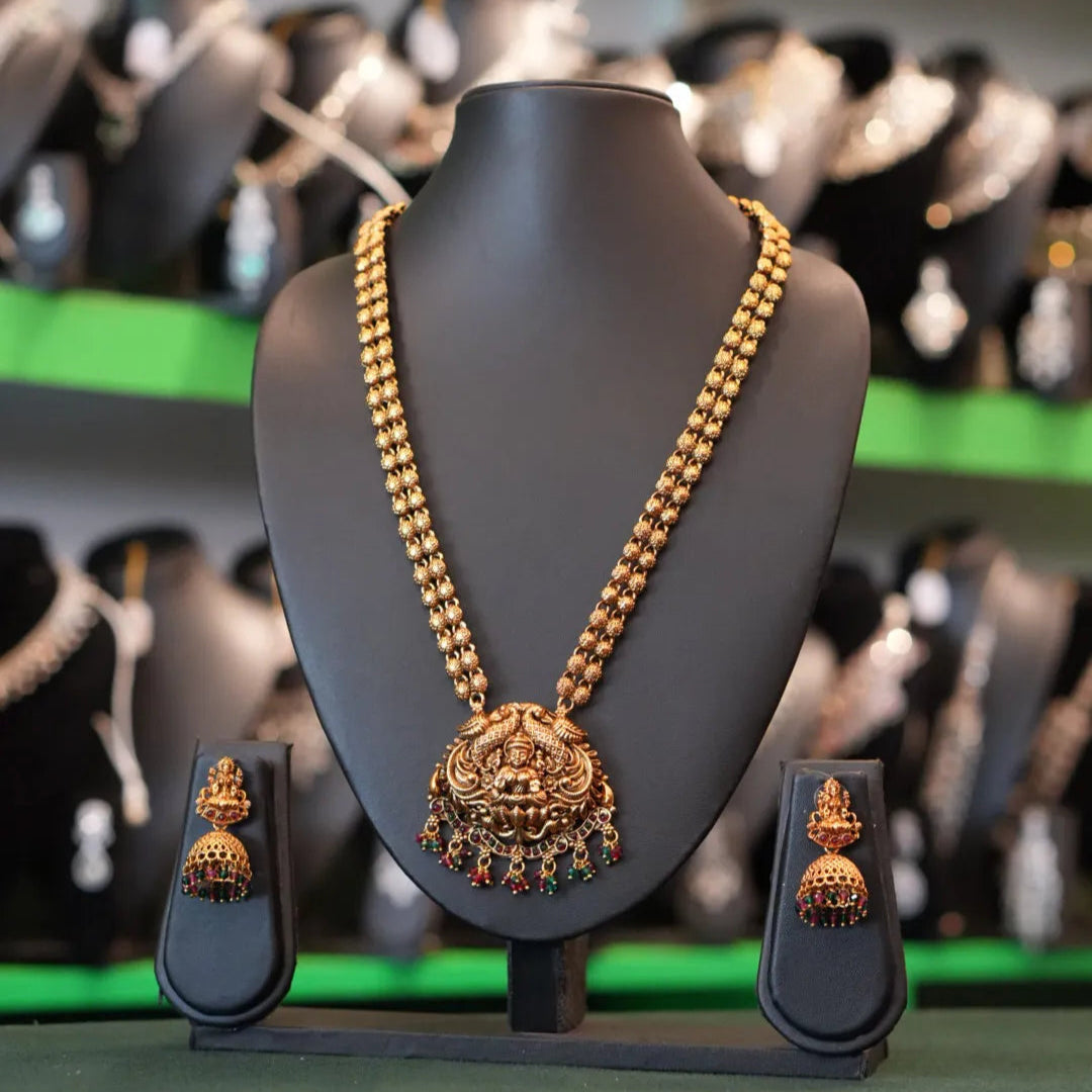 Gold necklace and earrings on a mannequin bust with a blurred jewelry store background.