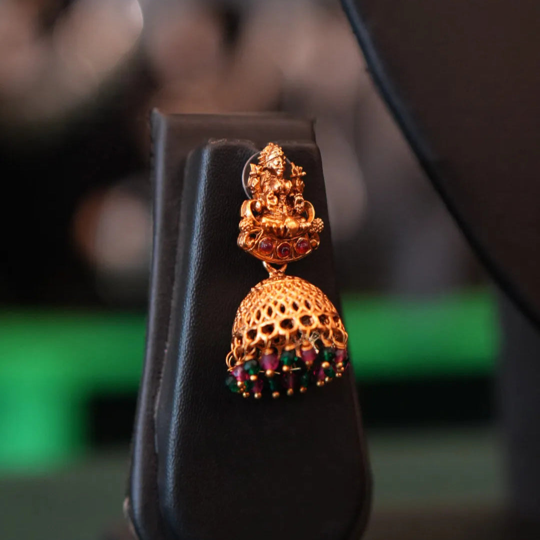 Gold earring with colorful stones on a black stand against a blurred background
