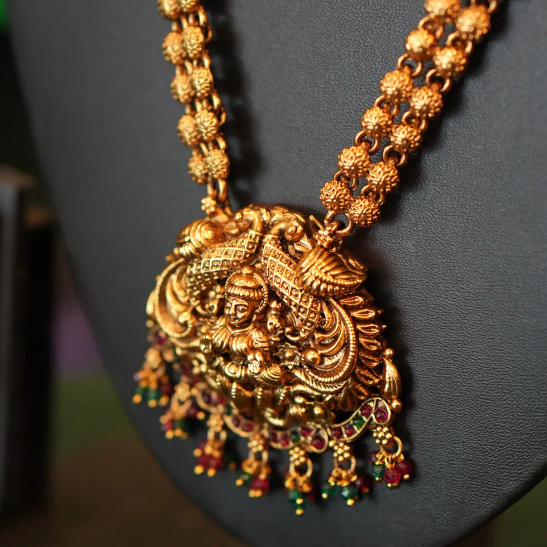 Gold necklace with intricate design and pendant on a dark gray stand