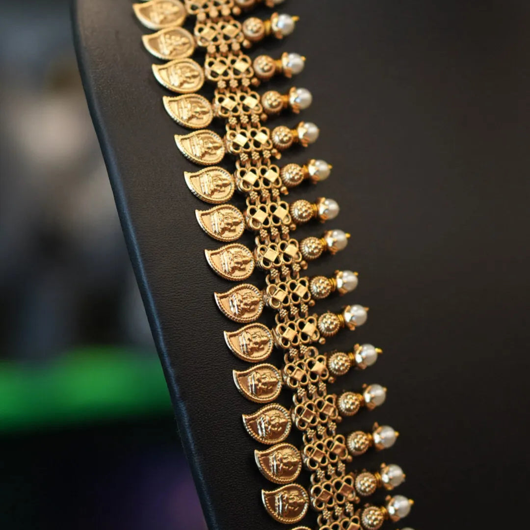 Gold necklace with pearl-like beads on a black stand against a blurred background