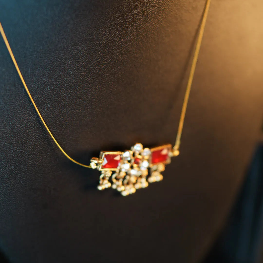 Gold necklace with a red and clear gemstone pendant on a dark background