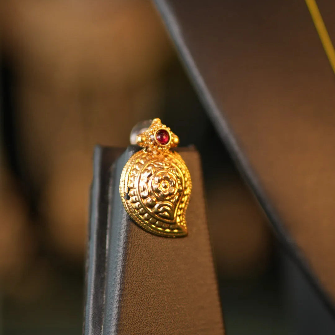 Gold earring with a red gemstone on a brown stand