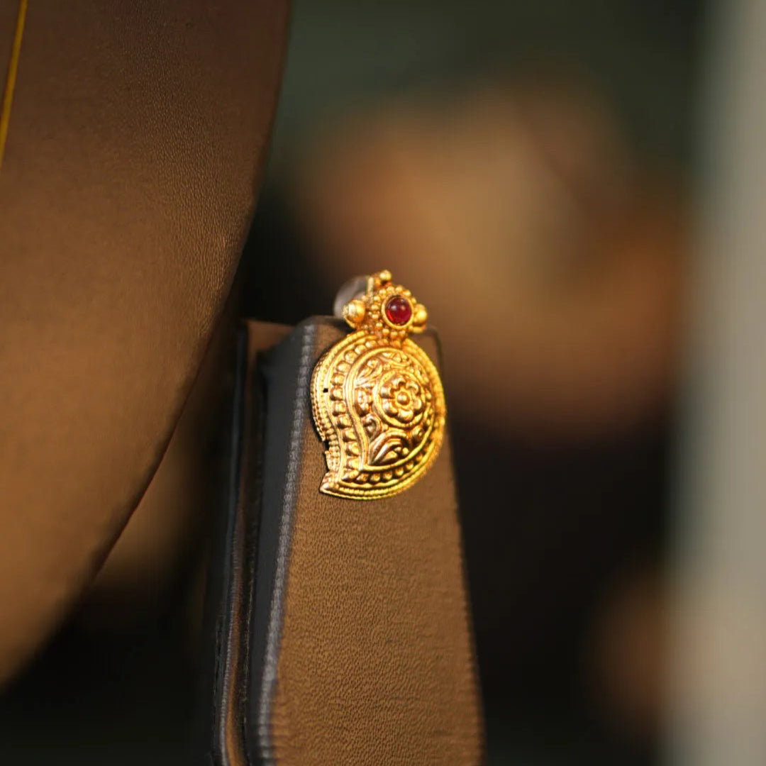 Gold shoe charm with a red gemstone on a brown shoe against a blurred background