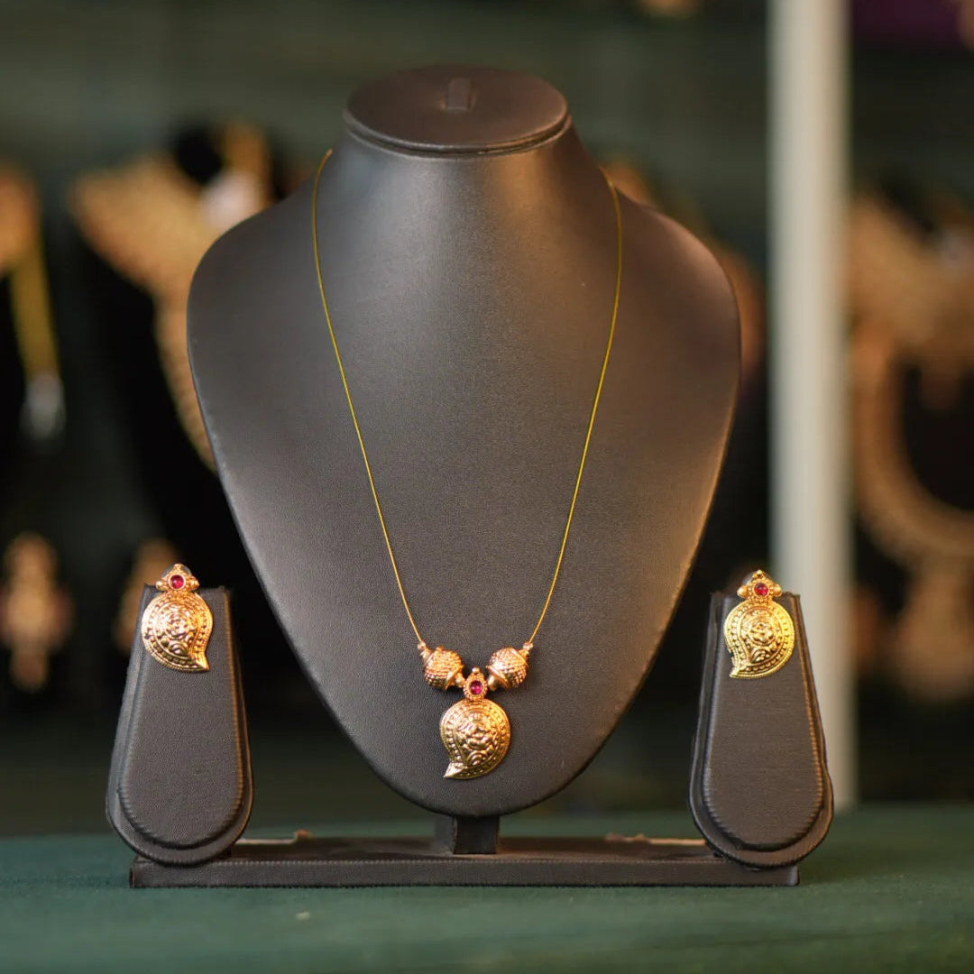Gold necklace and earrings on a black mannequin bust with a blurred jewelry store background.