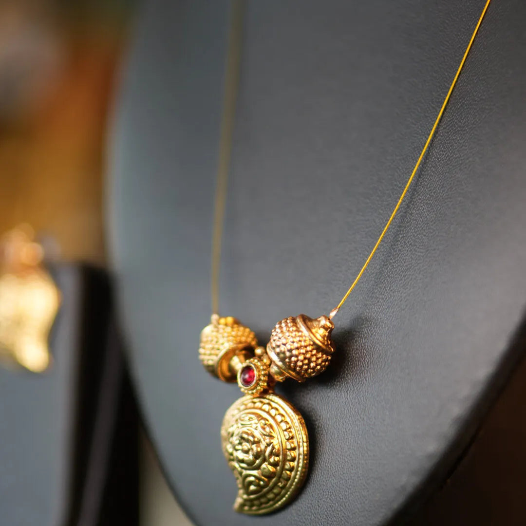 Gold necklace with intricate pendant on a gray stand
