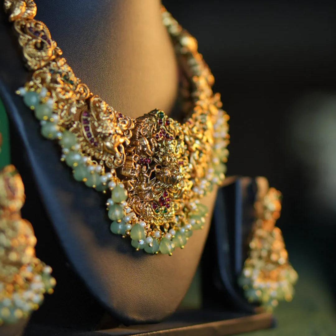 Ornate gold necklace with green beads on a mannequin bust.