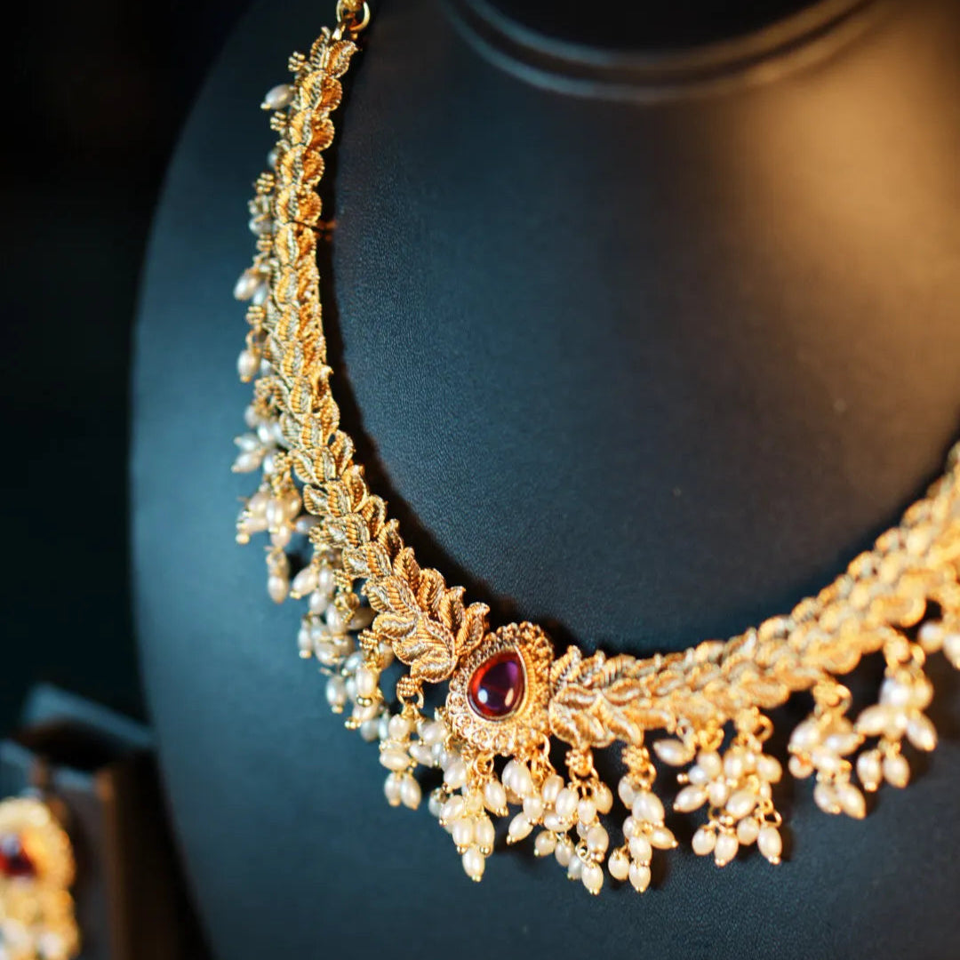Gold necklace with red gemstone on a black stand