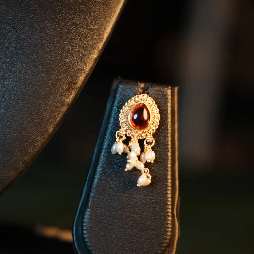 Decorative brooch with a red gemstone and pearl-like elements on a black background
