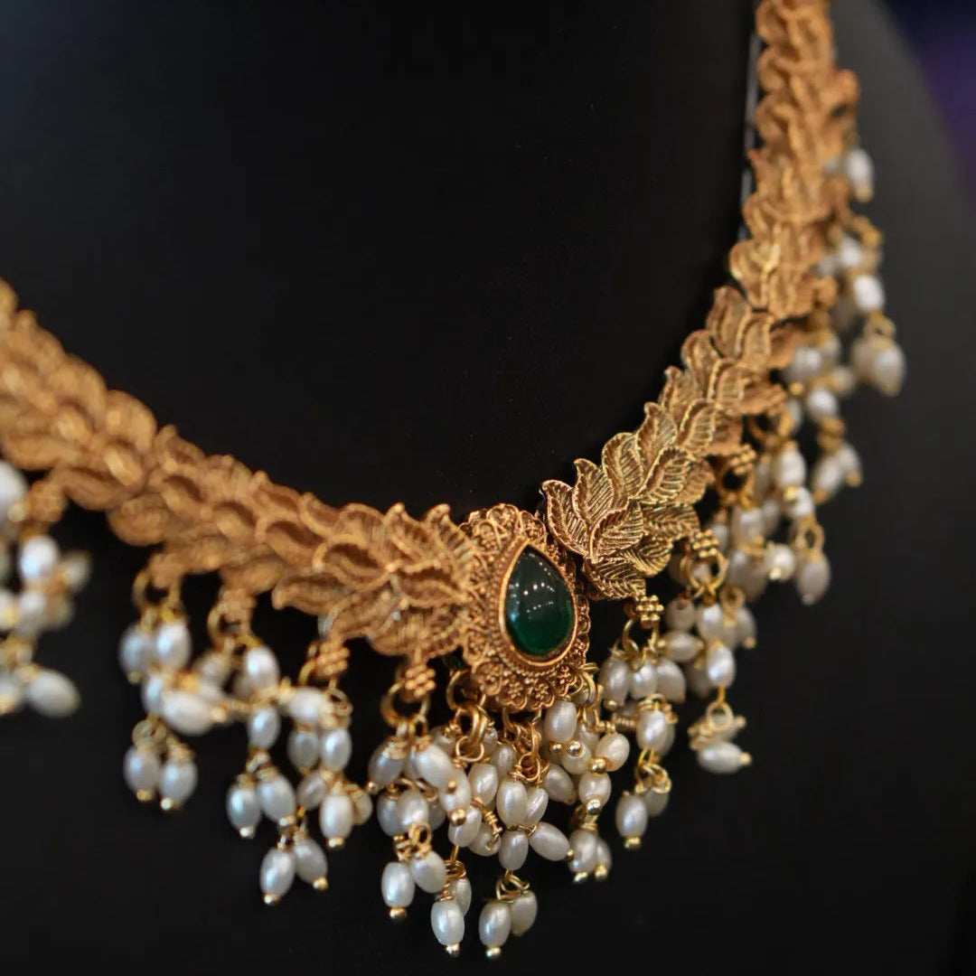 Gold necklace with pearls and a green gemstone on a black background