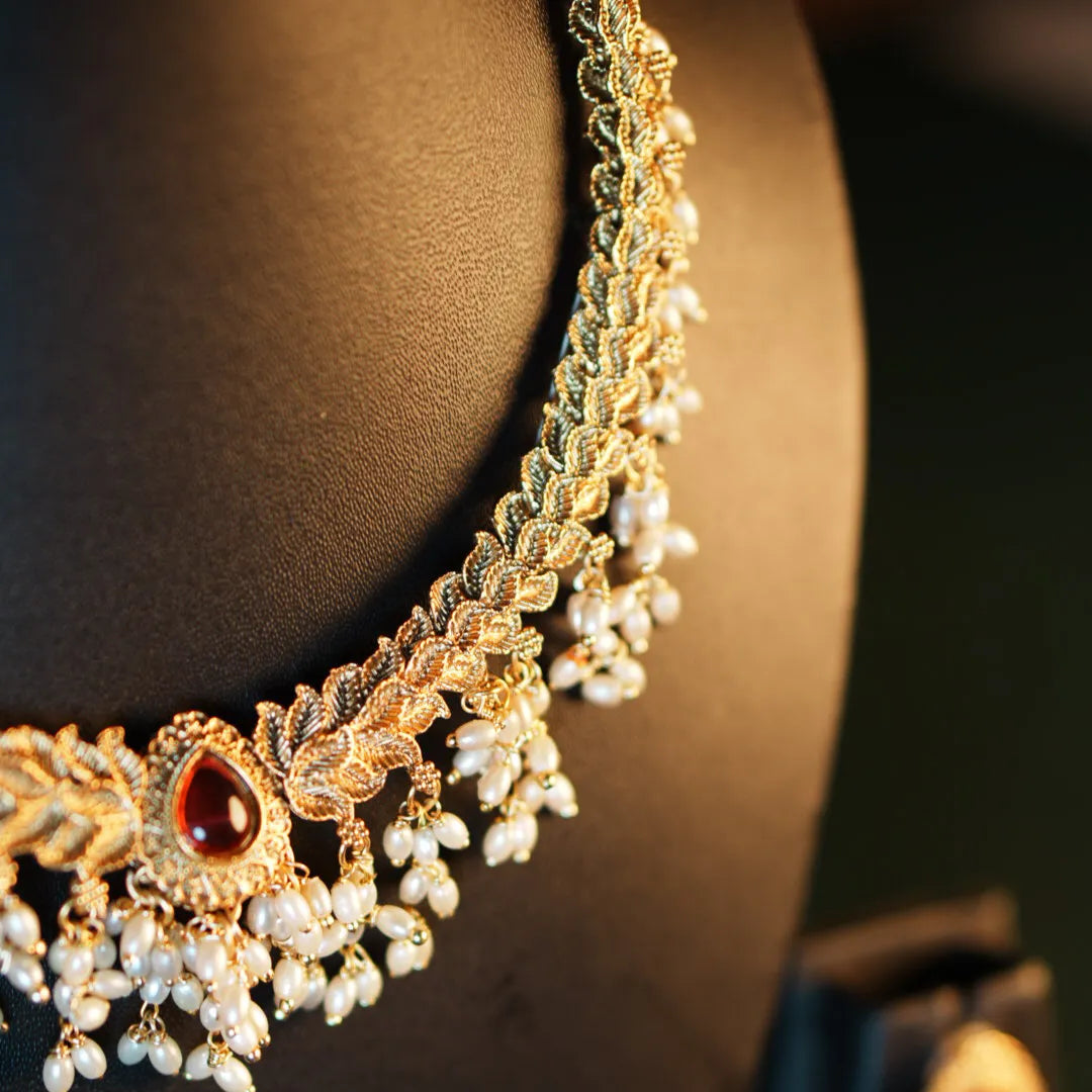 Gold necklace with red gemstone and pearl details on a mannequin.