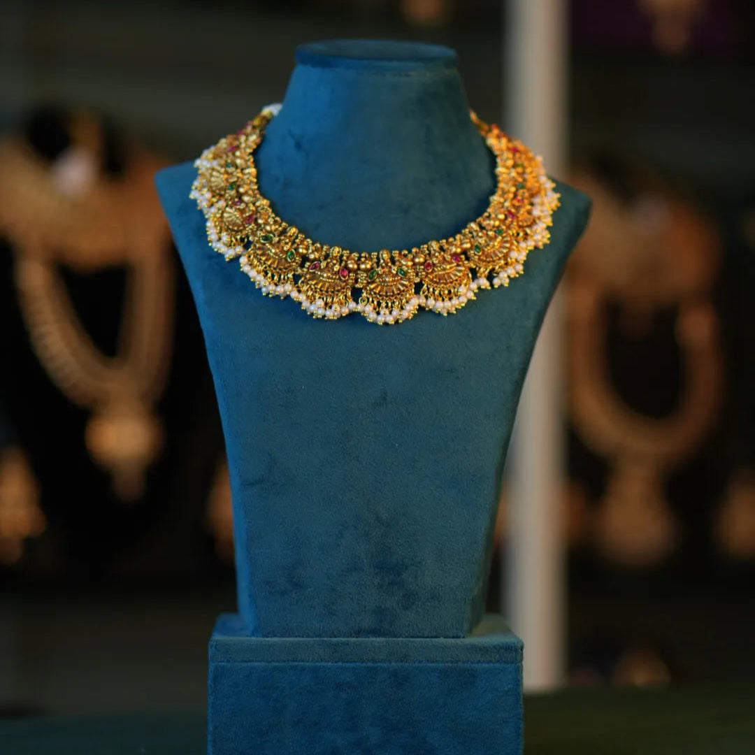 Gold necklace on a blue mannequin bust with blurred jewelry background