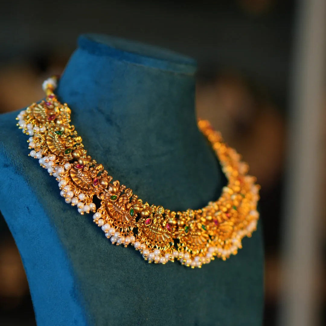 Gold necklace with red and green stones on a blue mannequin