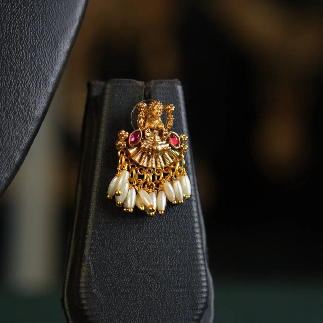 Gold and pearl earring on a black stand with a blurred background