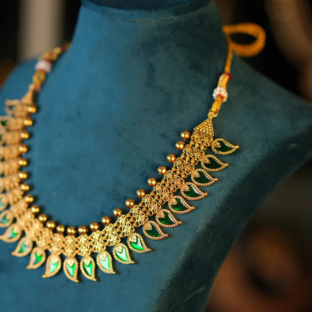 Gold necklace with green stones on a blue velvet mannequin