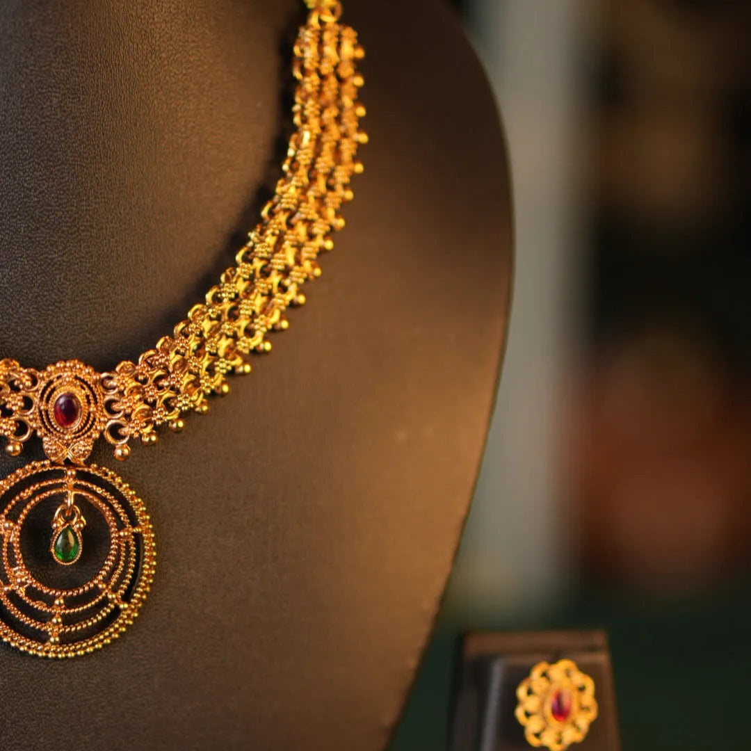 Gold necklace with red and green gemstones on a mannequin, blurred background