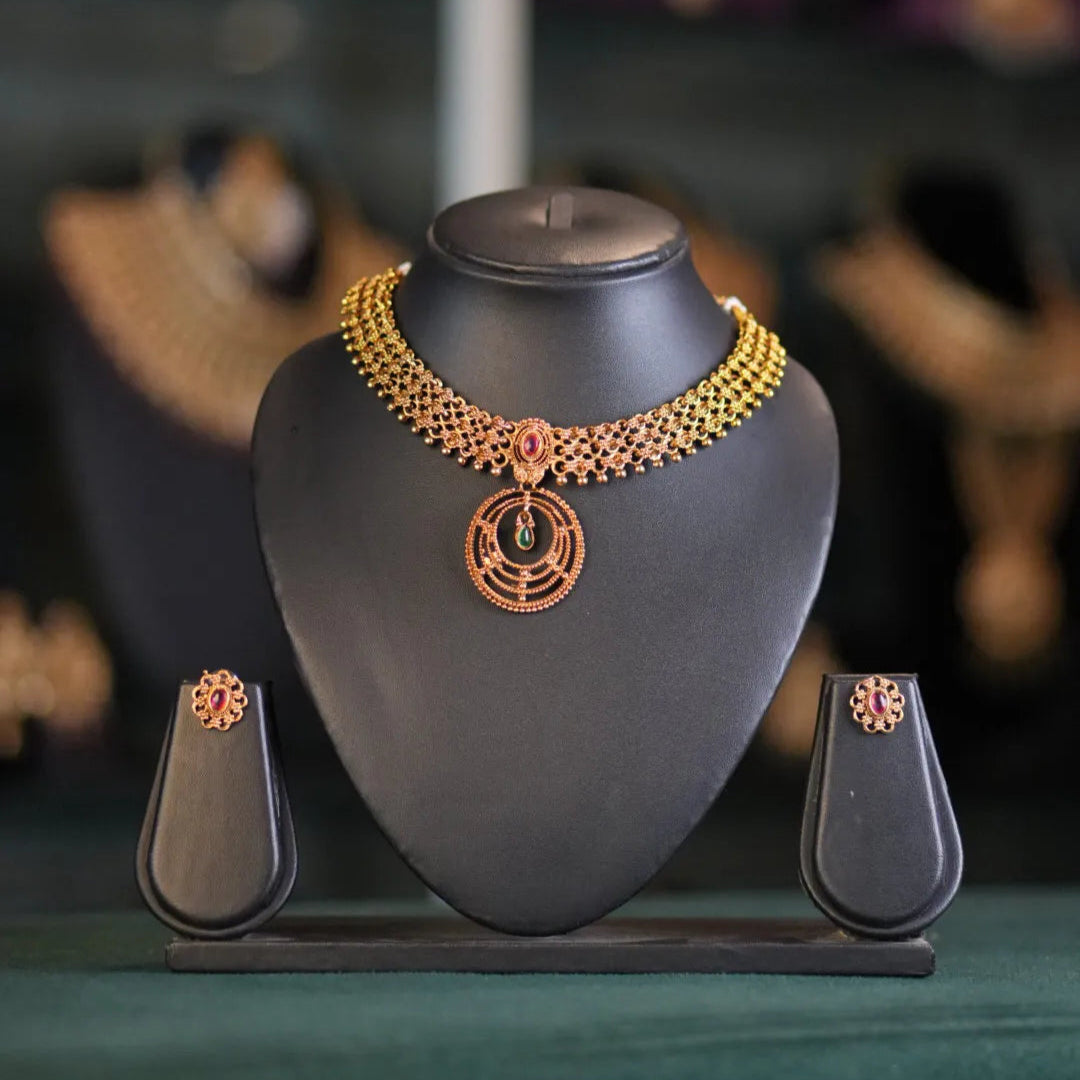 Gold necklace on a black stand with blurred jewelry in the background