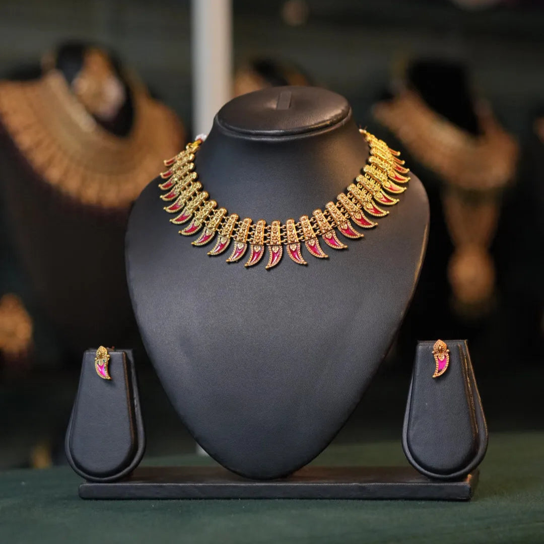 Gold necklace with pink stones on a black stand with earrings displayed below.