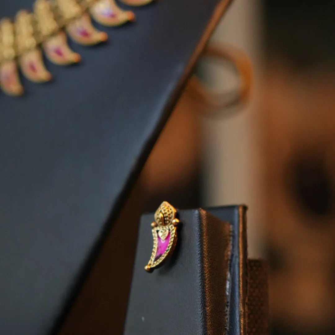Black leather pouch with decorative gold and pink pin on a blurred background
