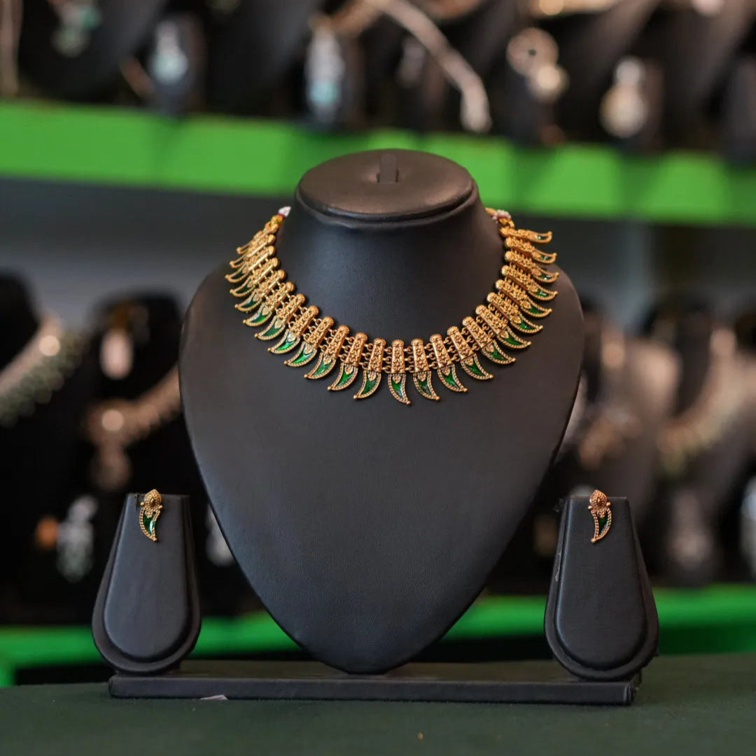 Gold necklace on a black stand with blurred jewelry in the background