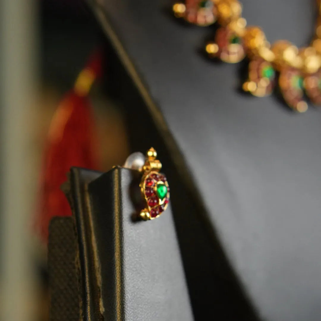 Close-up of a gold earring with a red gemstone on a black stand.