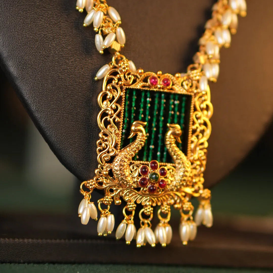 Ornate gold necklace with a green gemstone pendant on a dark background