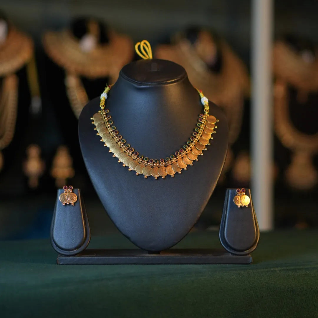 Gold necklace on a black mannequin bust with earrings on either side, against a dark background.