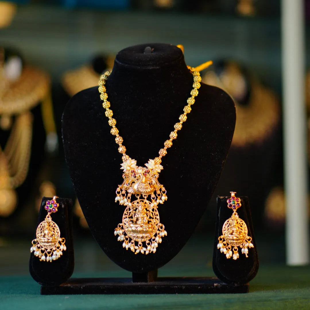Gold necklace and earrings set on a black mannequin bust with blurred background