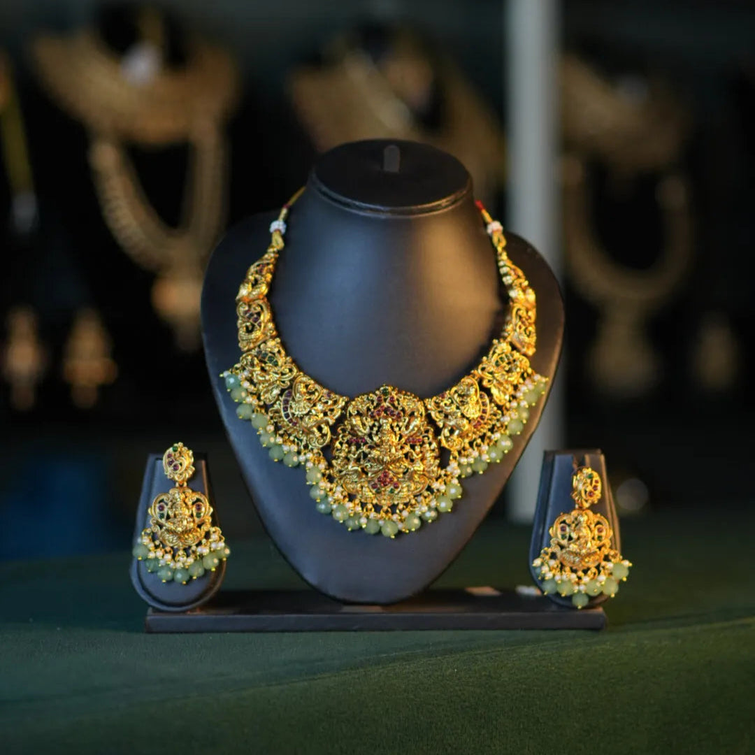 Gold necklace and earrings on a dark stand with a blurred jewelry store background
