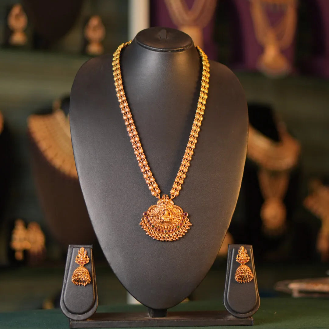 Gold necklace on a black mannequin bust with a blurred jewelry store background.