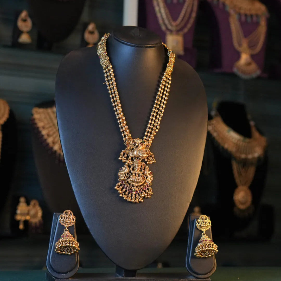 Gold necklace and earrings on a black mannequin bust with a dark background